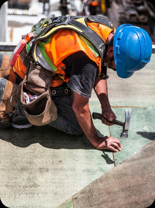 Tradesman Using Hammer on Construction Site A construction worker in an orange vest and blue helmet using a hammer on a floor.